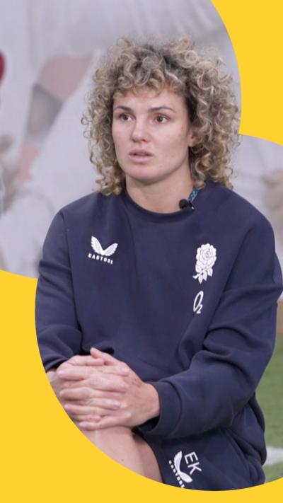 Ellie Kildunne wears a navy blue jumper and short set. She is sitting down and looks past the camera.