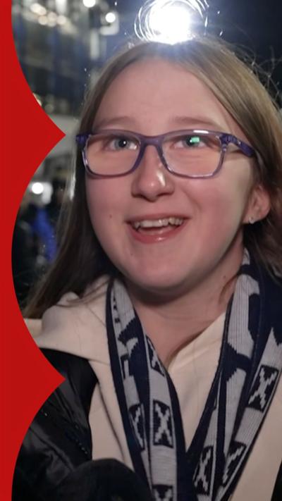A girl with long brown hair, glasses and a Scotland scarf 