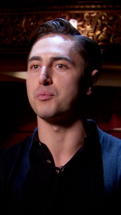 Connor Carson is standing on stage being interviewed. He has styled dark brown hair and a dark polo shirt.