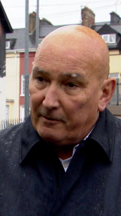A bald man in a black rain coat