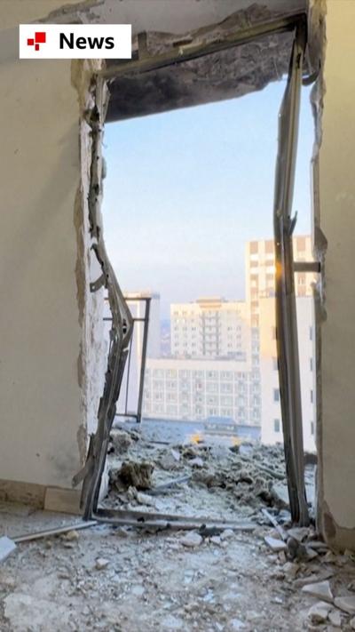 Looking out through a destroyed door. There is rubble on the floor and blue sky outside