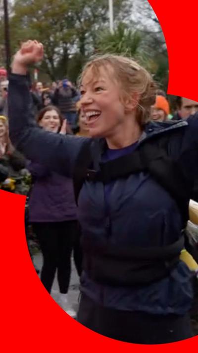 Sara Cox holds her hands up celebrating wearing a black jacket