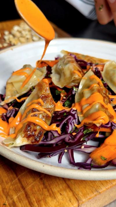 A close up of a plate filled with fried gyoza with an orange dressing drizzled over