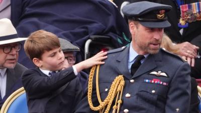 Prince Louis touches his dad William's shoulder as he wears military attire while sat next to him