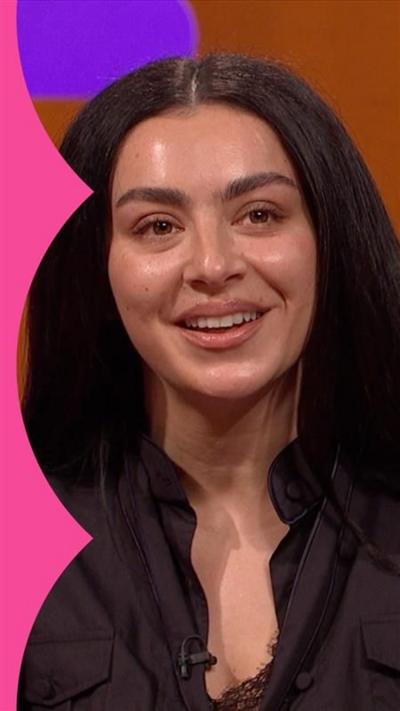 Charli XCX smiles. She has long black hair and wears a black shirt 