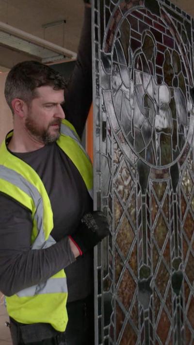 a man in a hi vis jacket holding a piece of stained glass