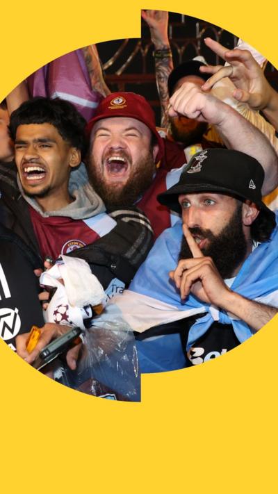 A crowd of Aston Villa fans cheering and waving their arms in the air in celebration at their team winning the Europa League.