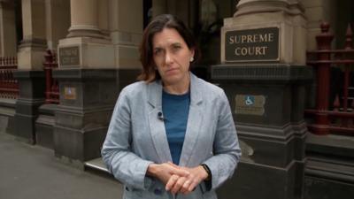 BBC correspondent Katy Watson standing outside the Supreme Court of Victoria. She is wearing a dark blue top and light blue blazer