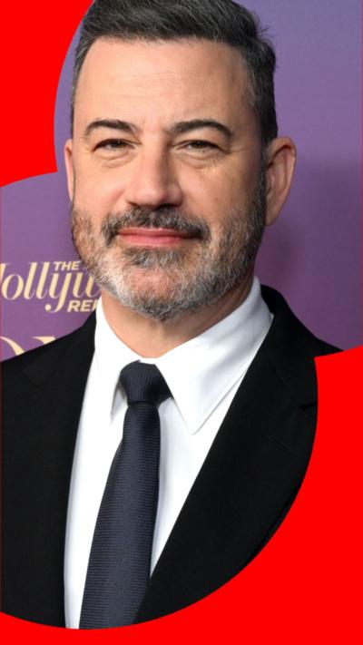 Jimmy Kimmel wearing a black suit with a white shit and a dark blue tie