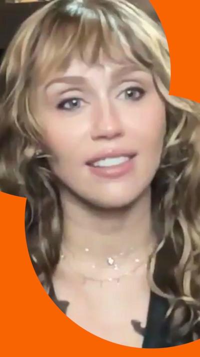 Miley Cyrus smiles during a video call - she has long wavy brown hair