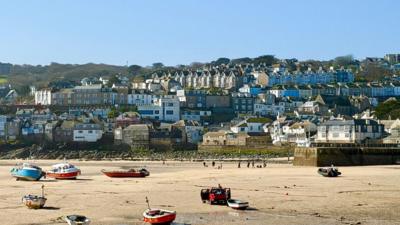 Small boats on a beach at low tide with houses behind and a blue sky above 