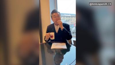 Japanese Ambassador eating Welsh cake with mug with Welsh dragon in other hand