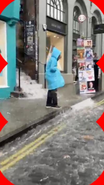 Woman in blue coat standing by cobbled street running with rain