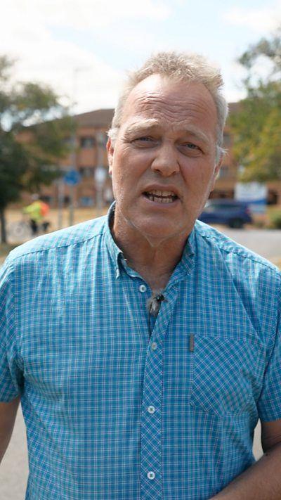 Reporter Matthew Hill in a blue checked shirt speaking outside into a camera.