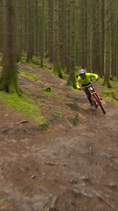 Teenager cycling on a dirt track with trees around him and a bright hi-vis jacket on.