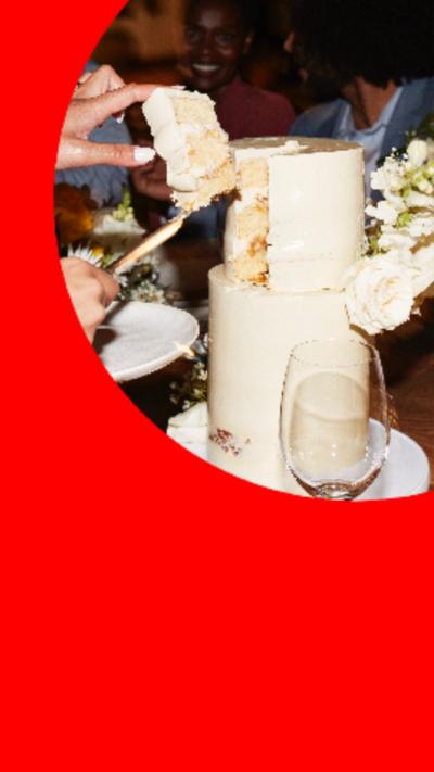 A wedding cake being cut with a wine glass next to it on the table.