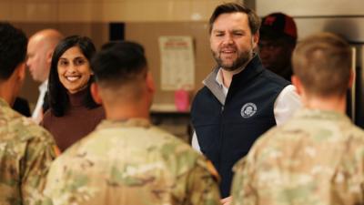 A woman and a man smiling facing soldiers in uniform with their backs to us. 