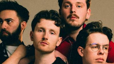 Four male members of a band. Two have beards and one is wearing glasses