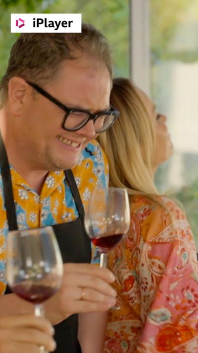 A man, Alan Carr, laughs as he holds a glass of red wine 