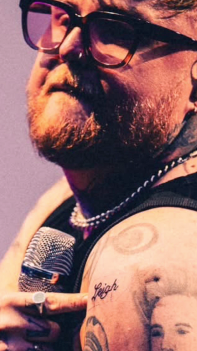 A man points at a tattoo that reads Leigh on his left after while holding a microphone