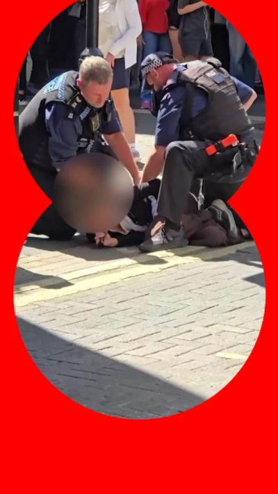 Two police men arresting a woman on the ground. Her face is blurred.