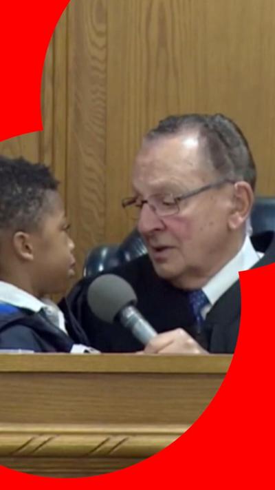 Screengrab of judge Caprio with a little boy on his lap in court, holding a microphone up to him 