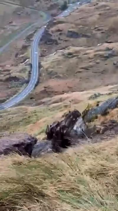 A boulder on a grassy hill with the A83 trunk road in the background.
