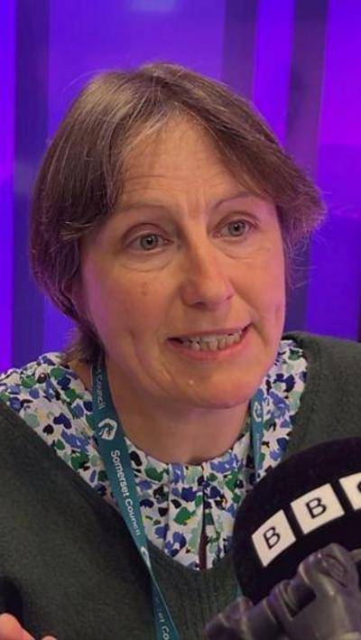 Woman with short brown hair speaking into BBC microphone.