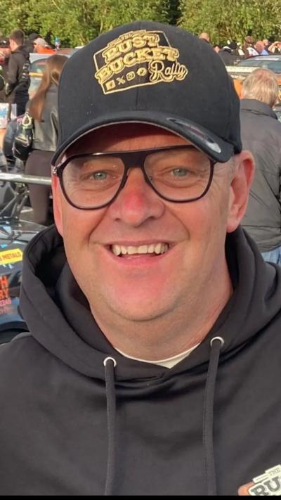 A man in a black hoody and black baseball cap smiles broadly at the camera.