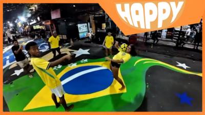 People doing football tricks on a street painted in Brazilian colours