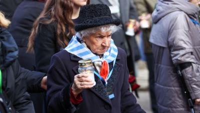 A former Auschwitz prisoner holds a candle as she approaches the 'death wall'