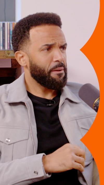 Craig David talks into a microphone  - he has short black hair and a beard, and wears a cream jacket