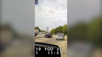 Screenshot of dashcam footage of a road with silver car in front of a roundabout.