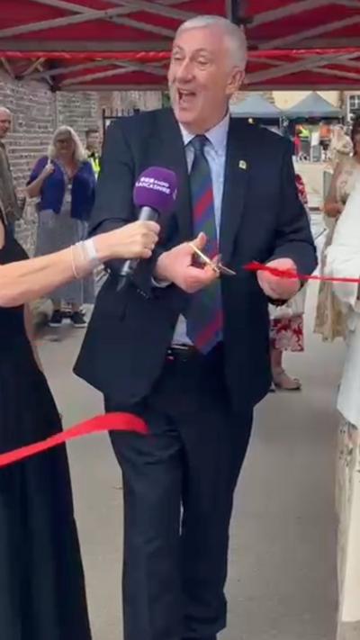 Man in a blue suit, shirt and tie cutting a red ribbon