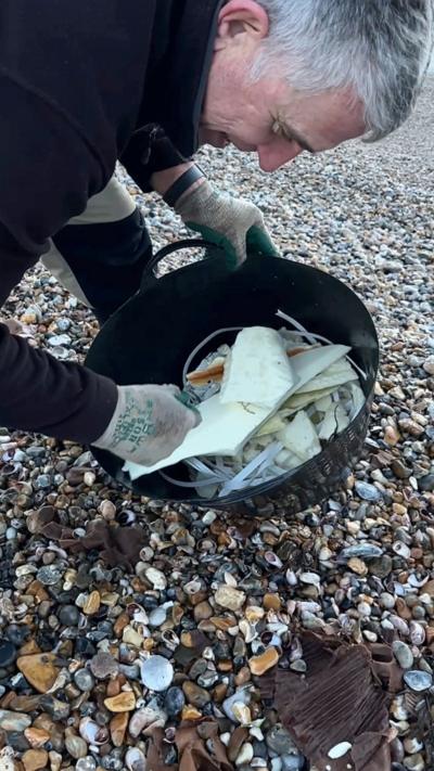 A man putting things into a bucket on the beach.