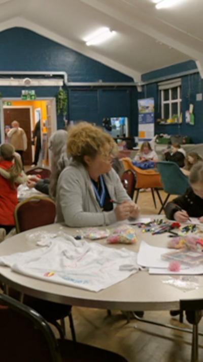 Young people inside a hall at a youth club sat around tables.