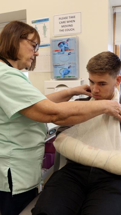 A man with his arm in a brace with a nurse seeing to him