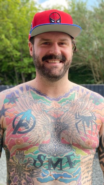 Man with tattoos over torso wearing a red hat