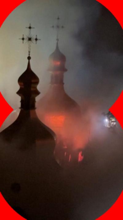 At night, fire glows on the cathedral roof as firefighters on a long ladder spray water on the site.