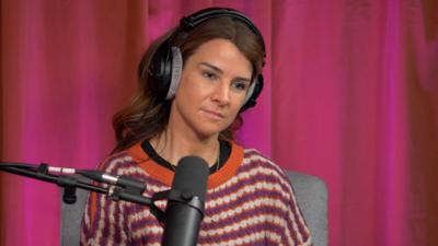 Izzy Judd, wearing a striped jumper and headphones, sitting behind a microphone