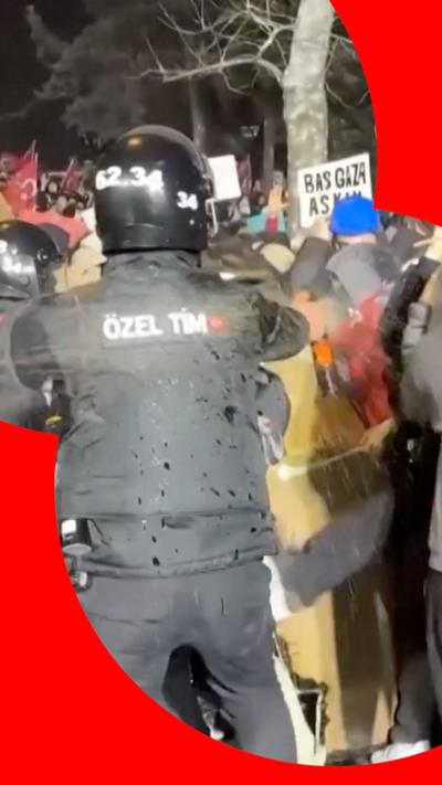 A police officer wearing PPE faces a crowd of protesters