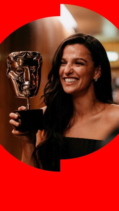 Marisa Abela smiles while holding her Bafta TV trophy - she has long brown hair and wears a sleeveless dress
