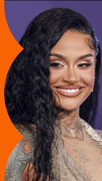 Kehlani, with long black hair and shoulder tattoos, smiles to camera, against a purple background