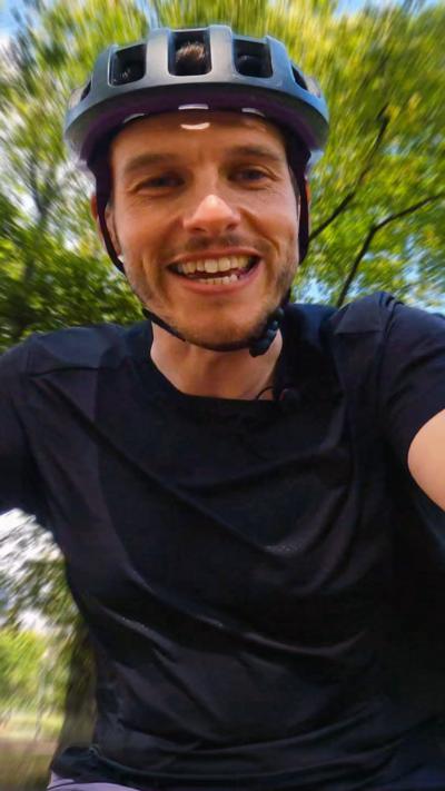 Man with wearing black cycle helmet and black T-shirt looking at camera and holding onto handle bars