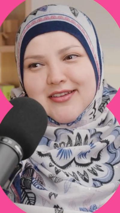 A woman in a blue and pink floral headscarf smiles into a microphone.