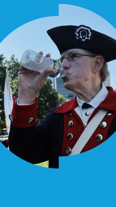 A US colonial era re-enactor in period costume drinks form a water bottle on a sunny day.