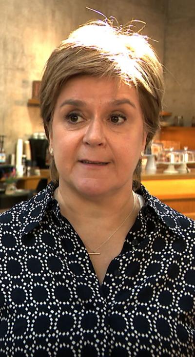 Nicola Sturgeon stands in the lobby of the Scottish Parliament, she wears a black and white top