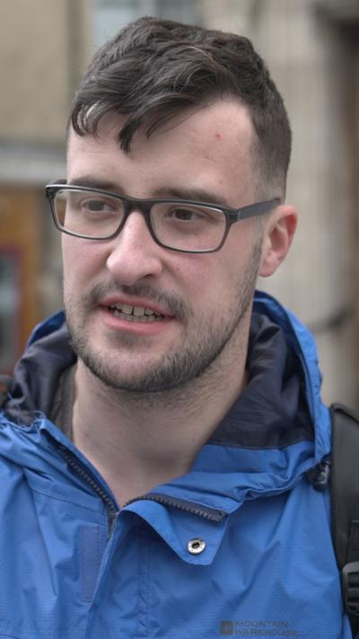 A man in a blue raincoat with dark hair and glasses