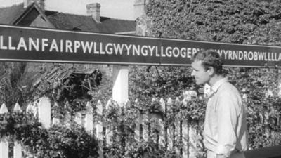 A reporter looks at a sign for Llanfairpwllgwyngyllgogerychwyrndrobwllllantysiliogogogoch.