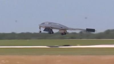 A grey war plane as it lands on a runway in a green field